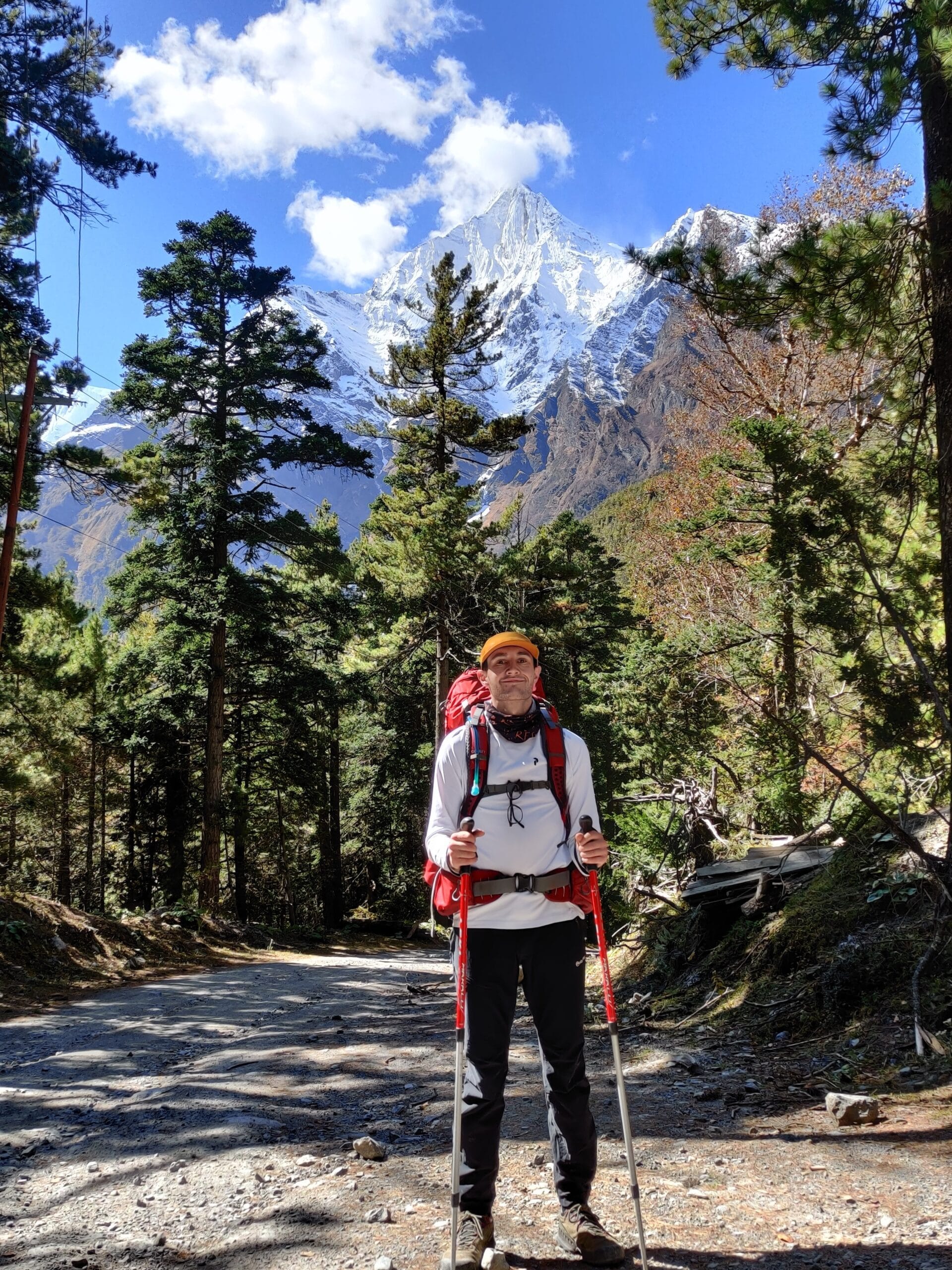 A Trekker carrying the Osprey Atmos AG Backpack with trekking poles in front of Annapurna 2