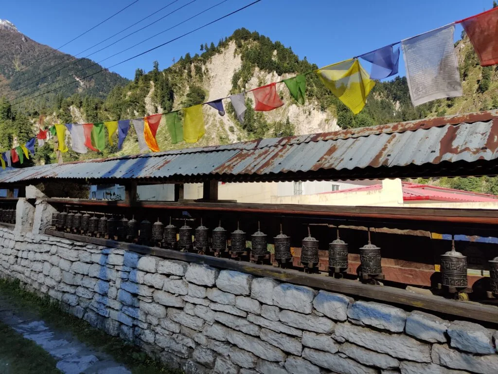 A wall with mani prayer wheels aligned with prayer flags above in a small village on the Annapurna Circuit