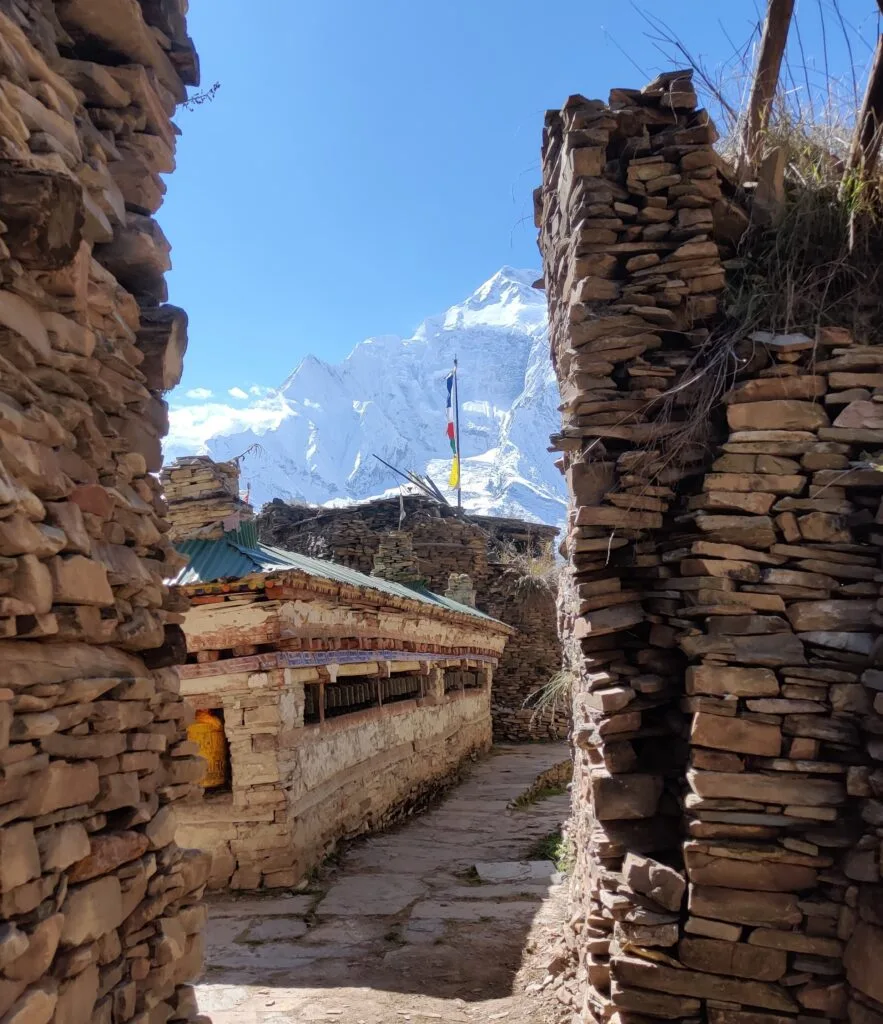 Narrow stoned alley and buildings with snow capped mountains of Annapurna 2 behind on the Annapurna Circuit