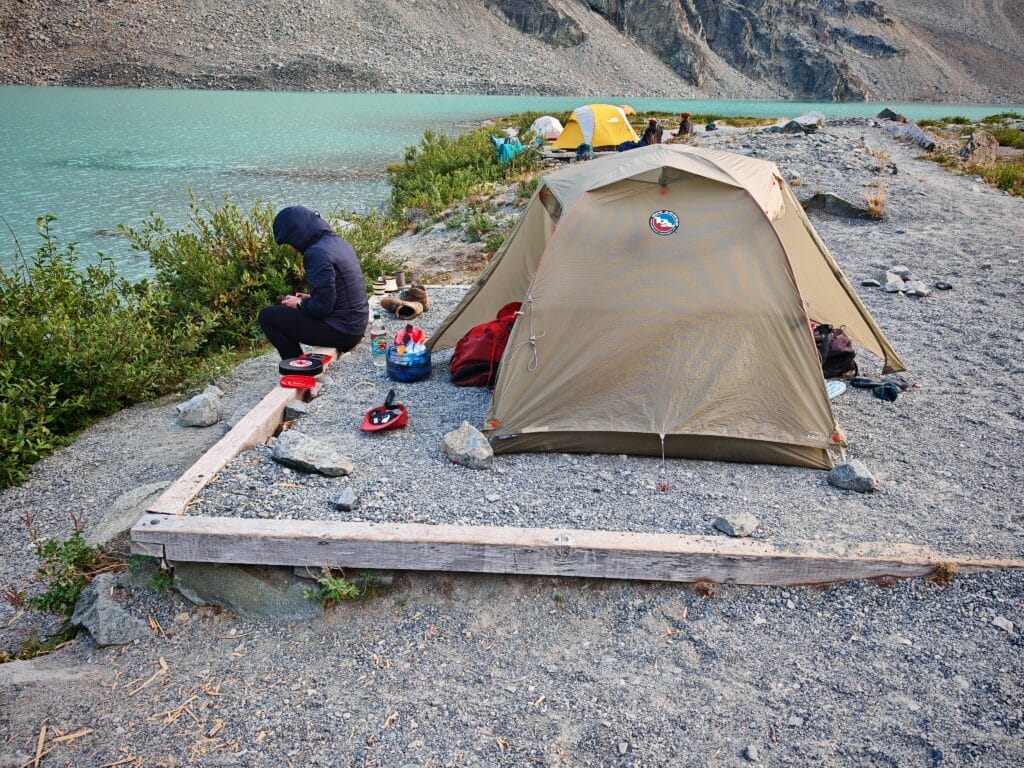 A backcountry campsite next to pitched Big Agnes Copper Spur  HV UL2 with cooking equipment and trekking kit laid out