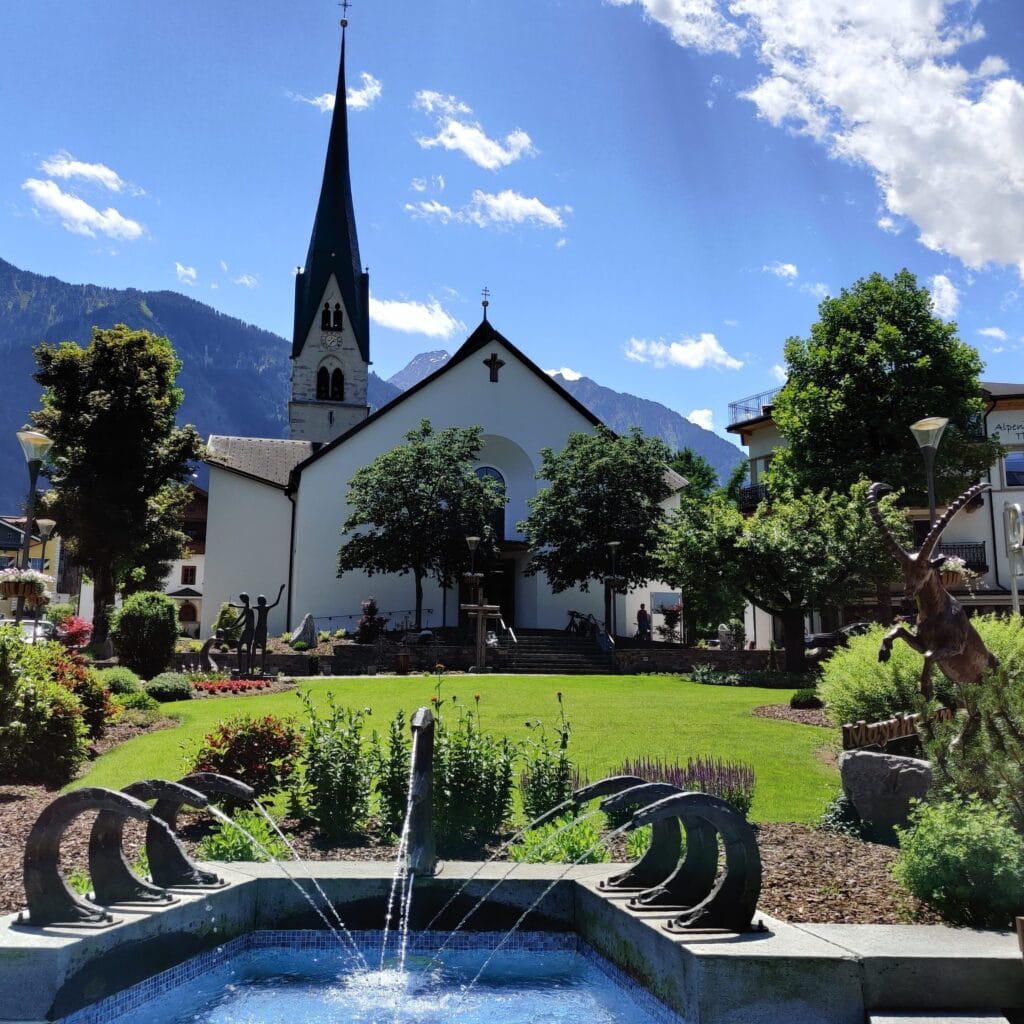 The central church in the Mayrhofen Village shows lush green plants and blue skies with a mountainous backdrop