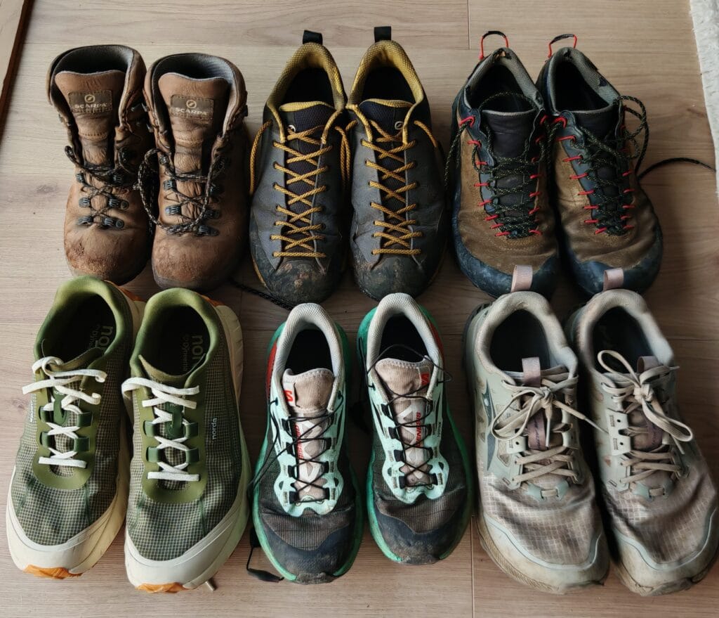 A collection of outdoor mountain shoes used in the hiking gear list including hiking boots, approach shoes and trail running shoes on a wooden floor. 
