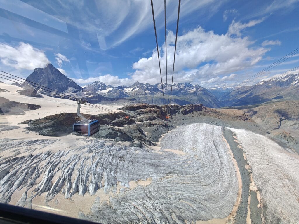 Aerial view from the Matterhorn Glacier Paradise cable car showing a gondola passing over a crevassed glacier toward the Matterhorn peak in Zermatt.