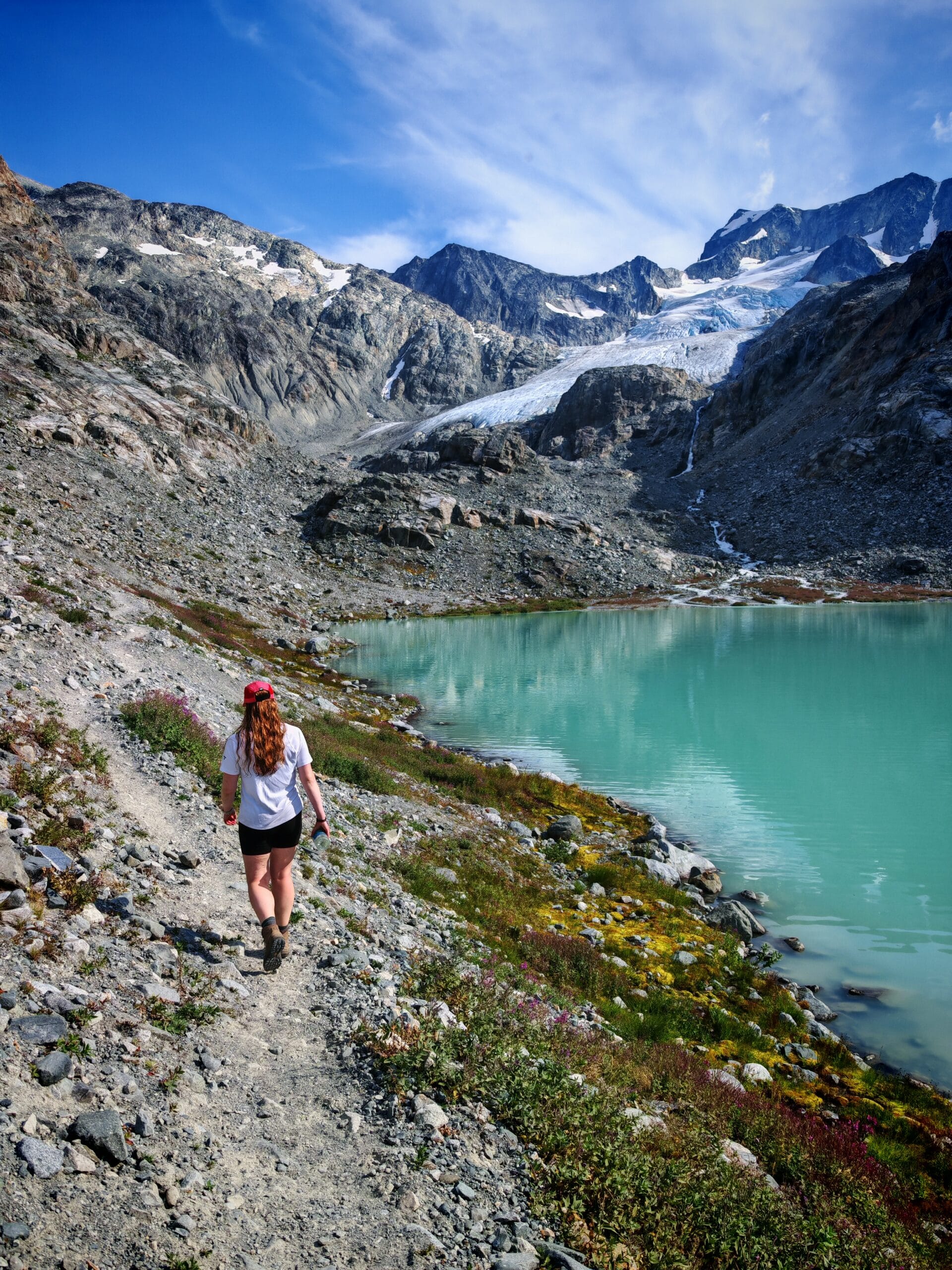 A female hiker on a stony trail towards Tupper Lake with Wedgemount Glacier in the background