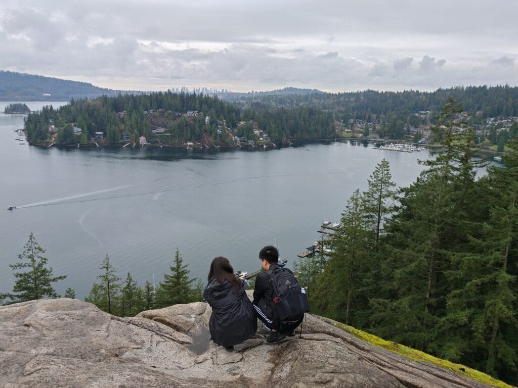 two hikers crouched on Quarry rock looking out over Deep Cove and Indian Arm waters in North Vancouver