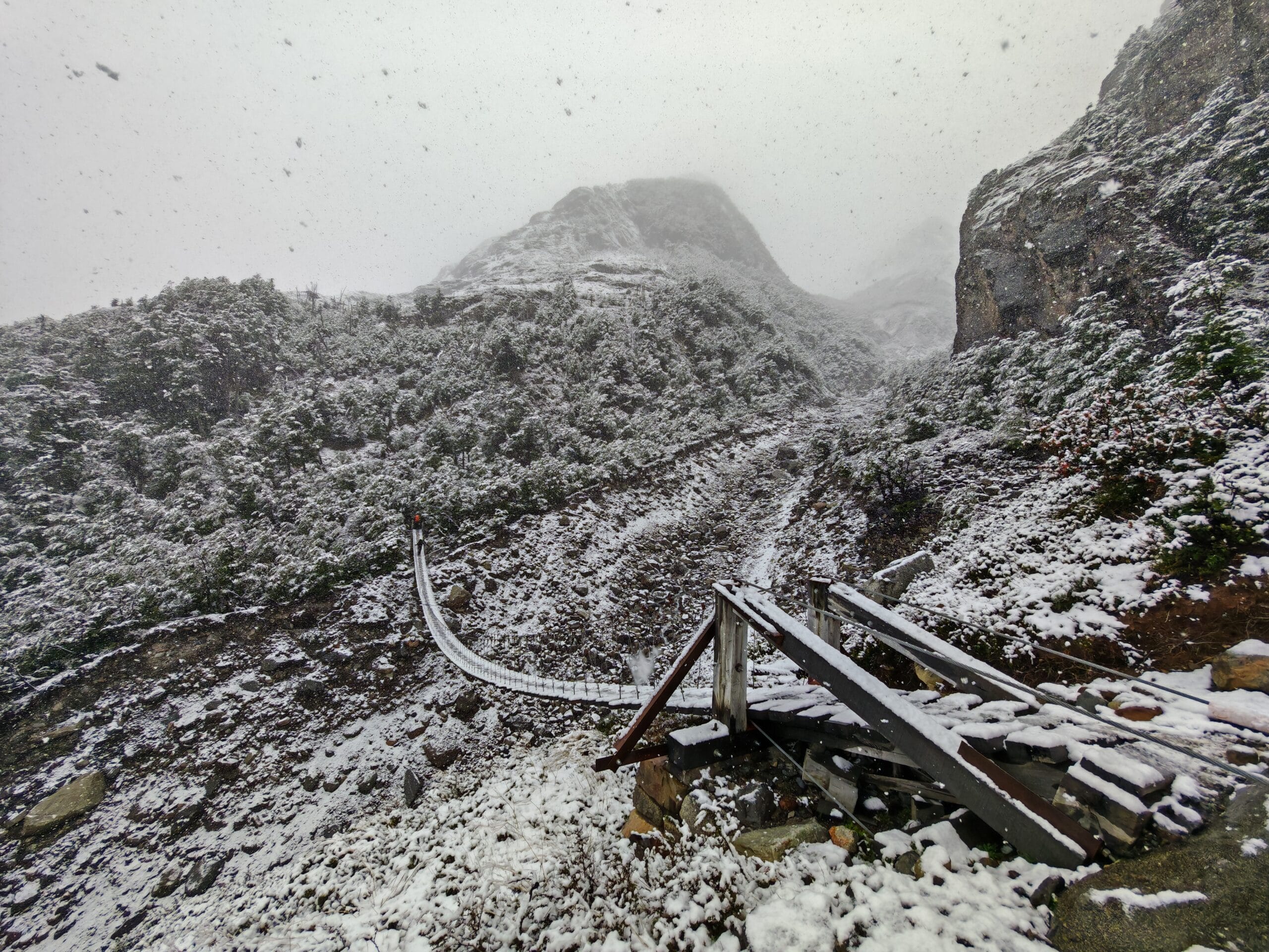 A wooden suspension bridge in a snowy hiking landscape bridges a steep ravine on the trail to grey Camp on the O Circuit