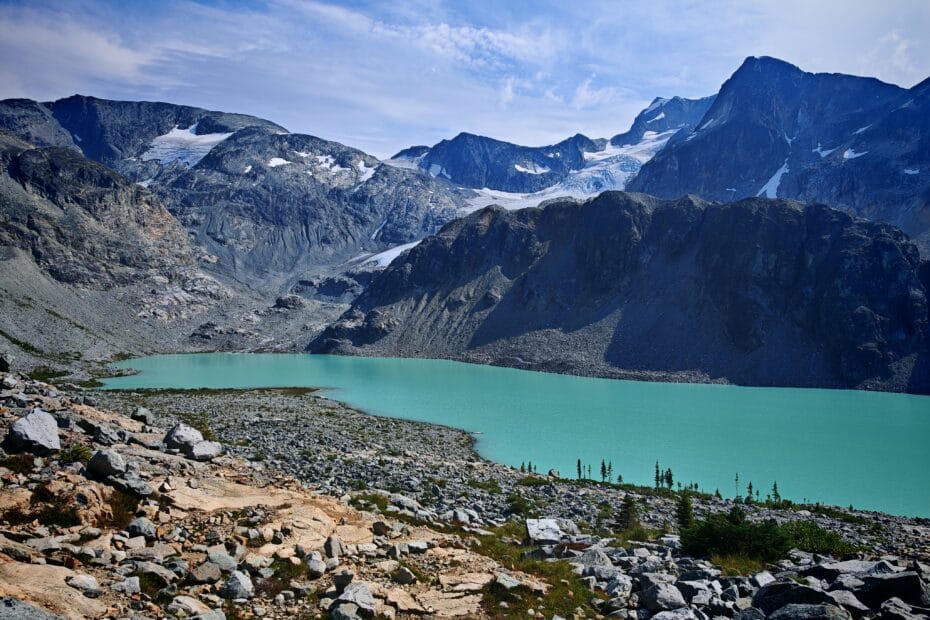 The turquoise waters of Wedgemount Lakes sits below rocky mountains surrounding the lake and with a rocky path seen in the foreground
