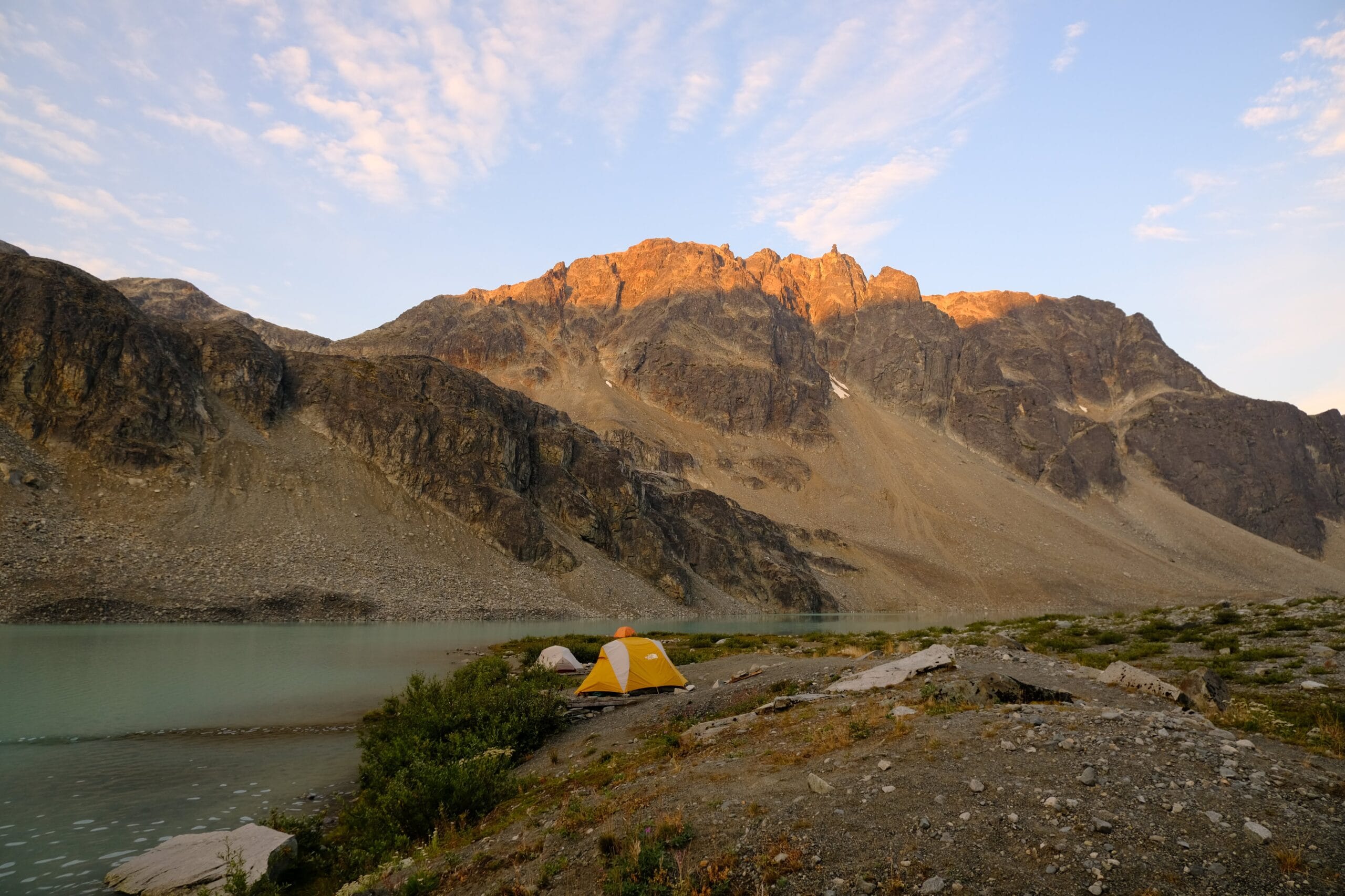 sunrise over the rocky mountain peaks with a yellow tent at upper Wedgemount Lake campground