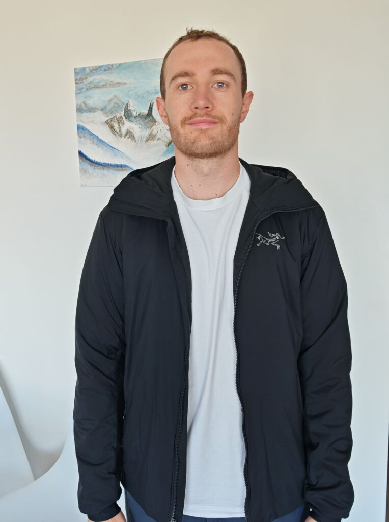 A man stood wearing the Arc'teryx Atom Hoody in Black size Small Men's against a white wall