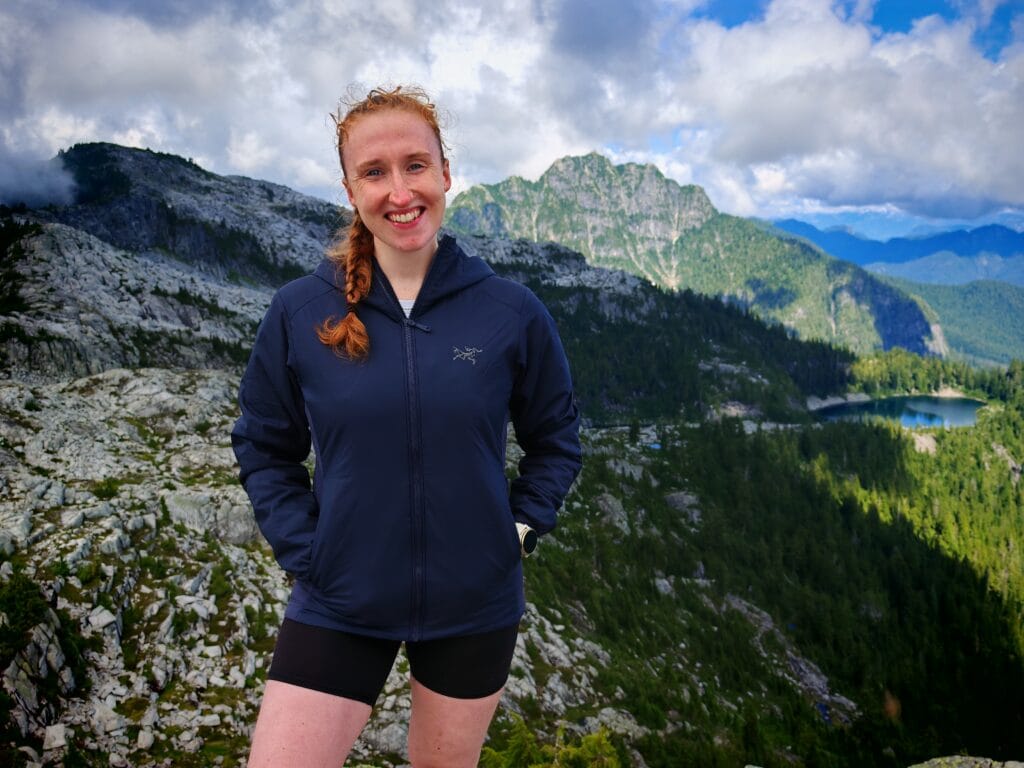 A hiker wearing the blue XS Arc'teryx Atom Women's Hoody jacket on a mountain summit in North Vancouver