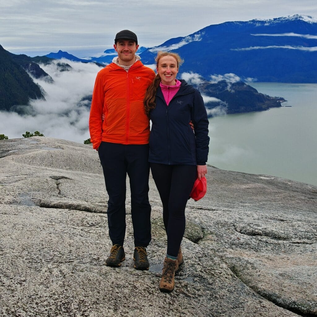 A hiking couple with the male wearing an orange Arc'teryx Proton LT Jacket and the woman wearing the Arc'teryx Atom Hoody on the summit of the Stawamus Chief in Squamish