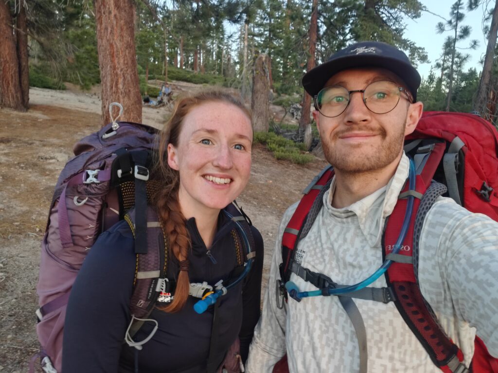 Backpacking Couple with male showing the magnetic valve of the Gregory 3D Hydro 3L Reservoir attached to Osprey Atmos AG 50 Backpack