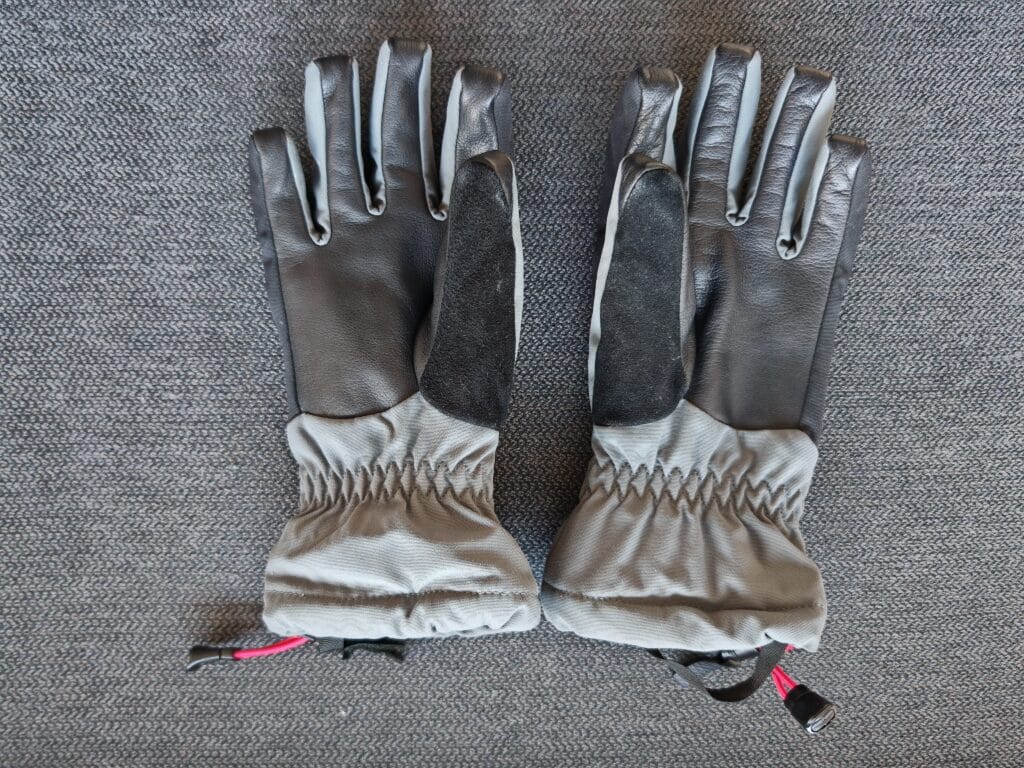 A pair of Mountain Equipment Guide Gloves facing up on a fabric background showing the leather palms and long cuff
