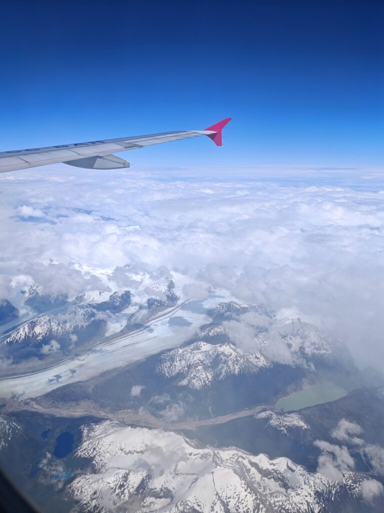 Airplane wing flying high above remote Patagonian icefields and mountains with clouds hiding the landscape below