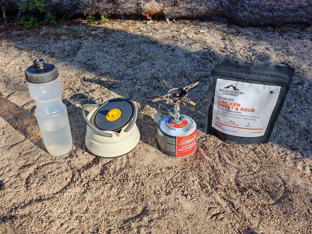 Camp cooking equipment and set-up with the soto windmaster, gas cansister, kettle, dehydrated meal and water in a wilderness campsite