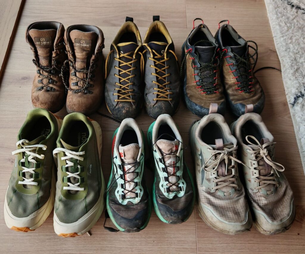line up of outdoor mountain footwear including from top left across: Scarpa Terra GTX boots, Scarpa Mescalito Planets, La Sportiva TX4 GTX. Bottom row left to right: Norda 002, Salomon Genesis women's and Altra Lone Peak 8