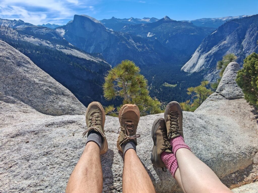 Pair of hikers showing their Norda 002 shoes and Arc'teryx Konseal Approach Shoes on Yosemite Peak with blue skies, granite mountains and trees in the valley below