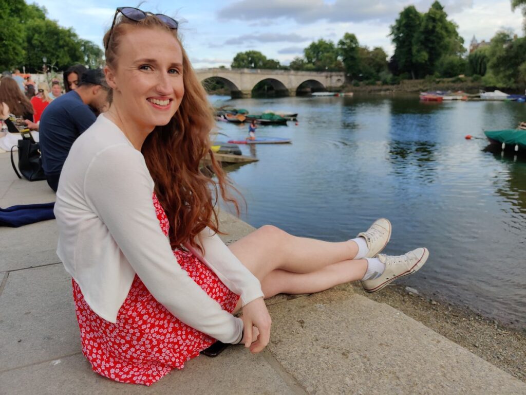 girl sat on the Richmond upon Thames riverside with Richmond Bridge in the background